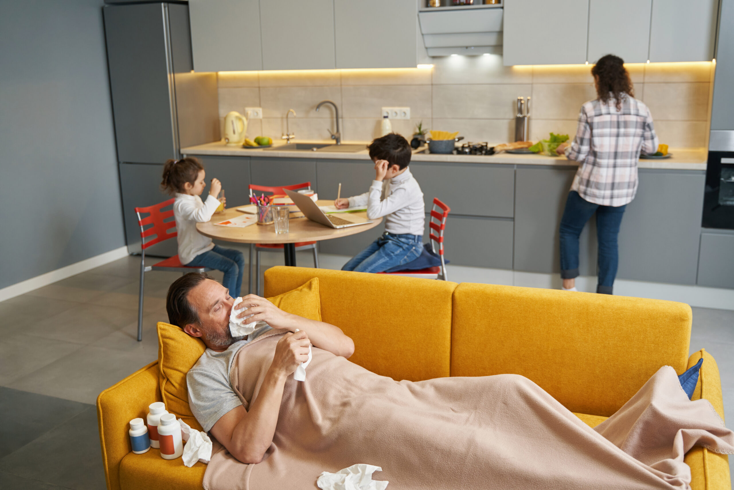 Ill male on sofa near his family in kitchen
